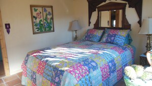 A bedroom with a wooden ceiling, a bed with a colorful quilt, a mirror above the bed, and a cactus plant on a side table. -  Casita Juliet in Taos, New Mexico (Taos)