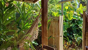 Una pérgola de madera con una hamaca, un banco de madera y exuberante vegetación tropical.
