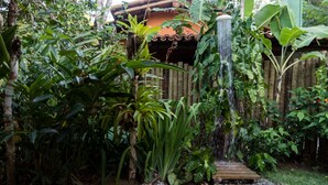 Un jardín con fuente de agua, terraza de madera y diversas plantas tropicales.
