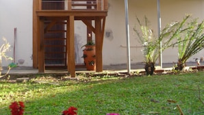 A wooden staircase leading to a balcony, surrounded by potted plants and a grassy area with flowers. - HOUSE IN THE MIDDLE OF NATURE (Florianopolis)