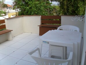 A patio with a white table and chairs, a bench, and a white wall with a window. - HOUSE IN THE MIDDLE OF NATURE (Florianopolis)