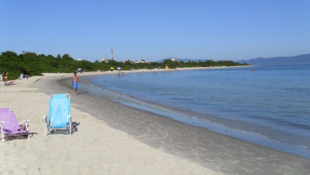 A beach with clear skies, a calm sea, and a few people. There are beach chairs and umbrellas visible. - HOUSE IN THE MIDDLE OF NATURE (Florianopolis)