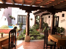 Un patio cubierto con vigas de madera, plantas en macetas y una mesa con sillas.