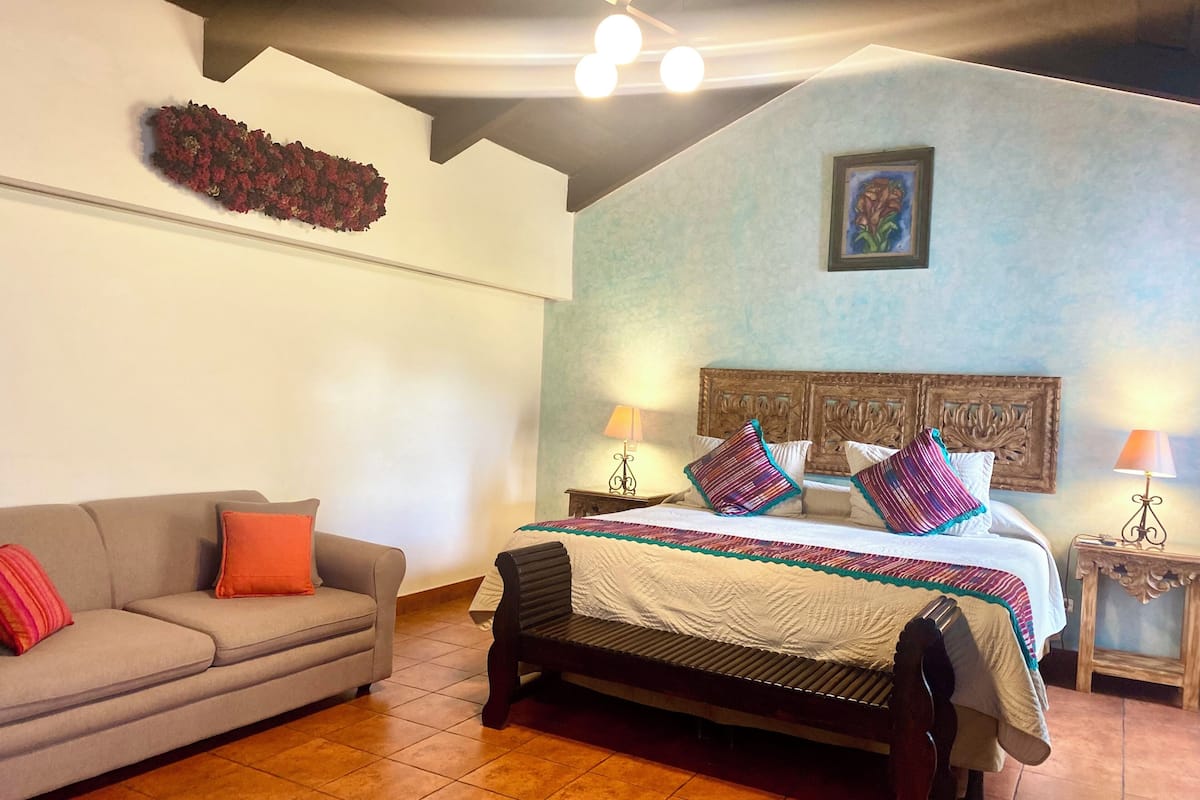 A bedroom with a bed, a sofa, and a nightstand with lamps.