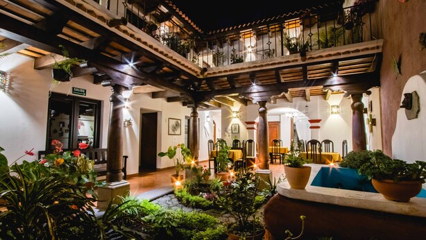Un patio con plantas en macetas, un área de comedor con mesas y sillas, y una escalera que lleva a un nivel superior.