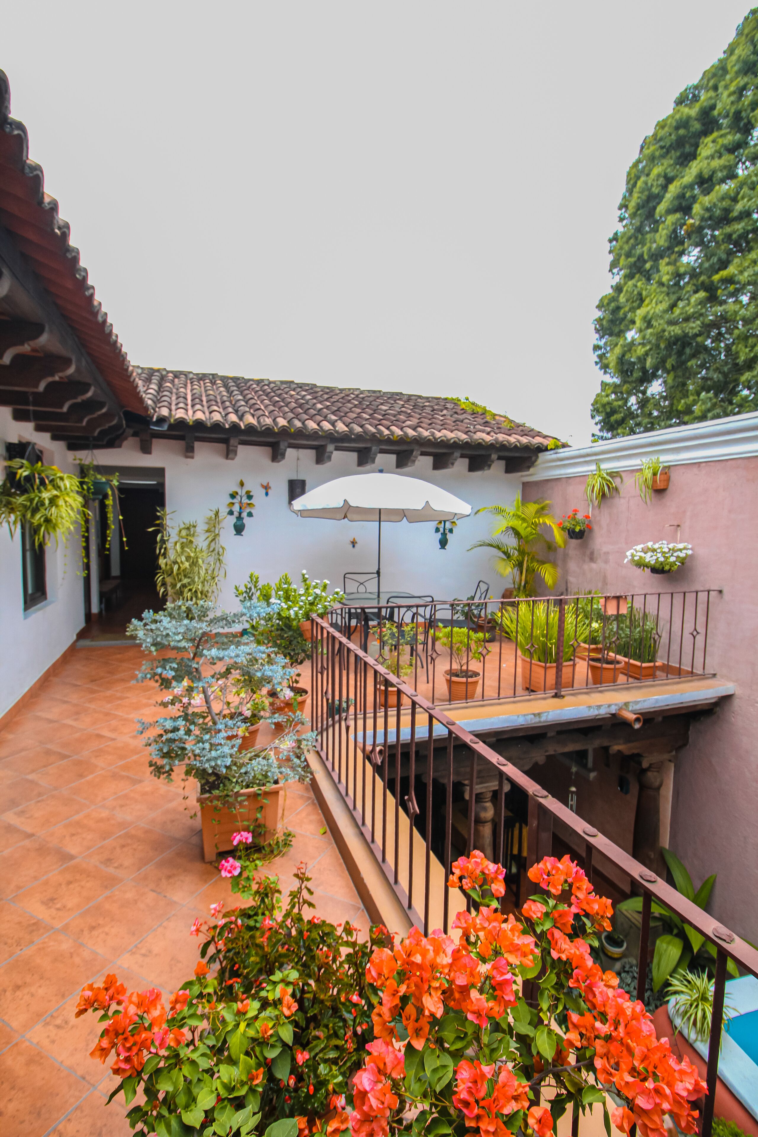 A courtyard with a tiled floor, potted plants, a table with chairs, and a railing.