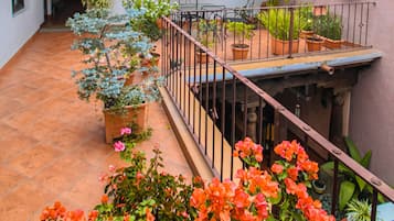 A courtyard with a tiled floor, potted plants, a table with chairs, and a railing.