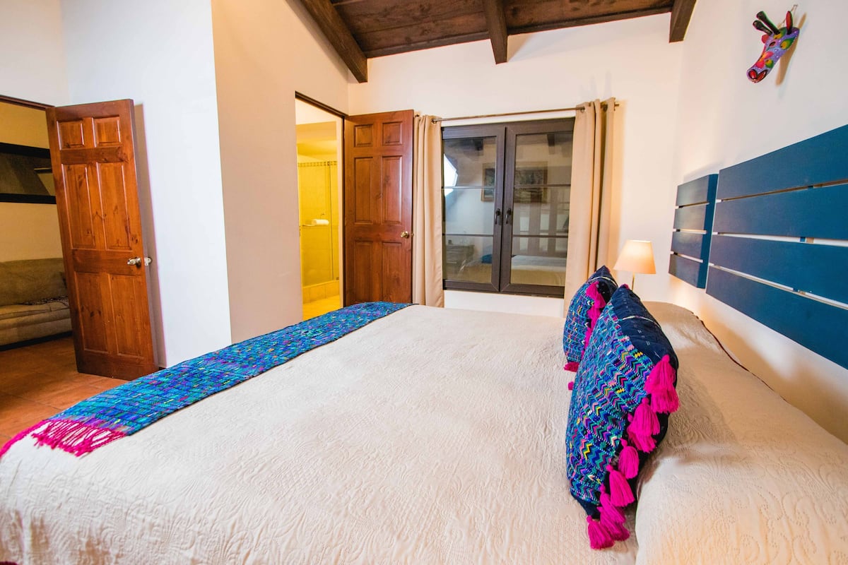A bedroom with a large bed, a wooden door, and a view through a glass door.