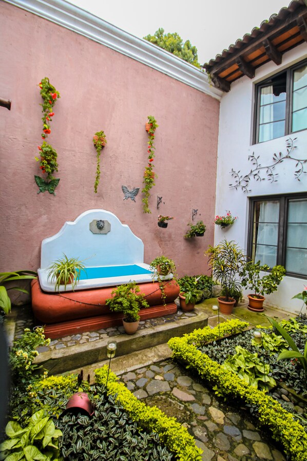 Un patio con un muro rosa, un banco blanco y diferentes macetas con plantas.