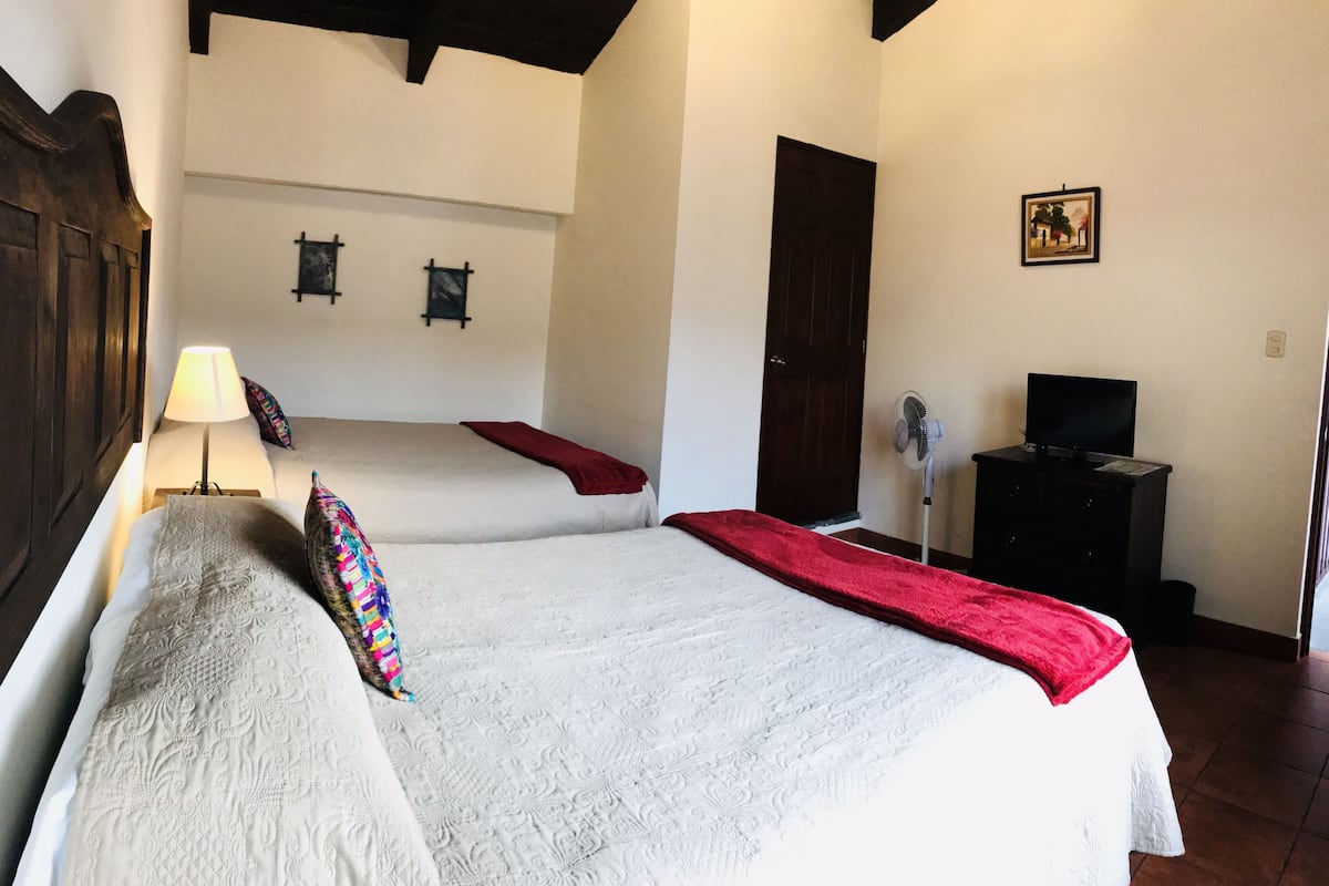 A bedroom with two beds, a TV, a fan, and a door.