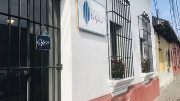 Fachada de hotel con cartel indicando que está abierto, una ventana con celosía metálica y vista a la calle con edificios coloridos.
