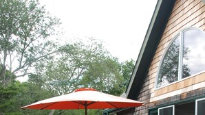 Une terrasse dotée de chaises et d’une table en bois, entourée d’une autre terrasse en bois et de portes vitrées.