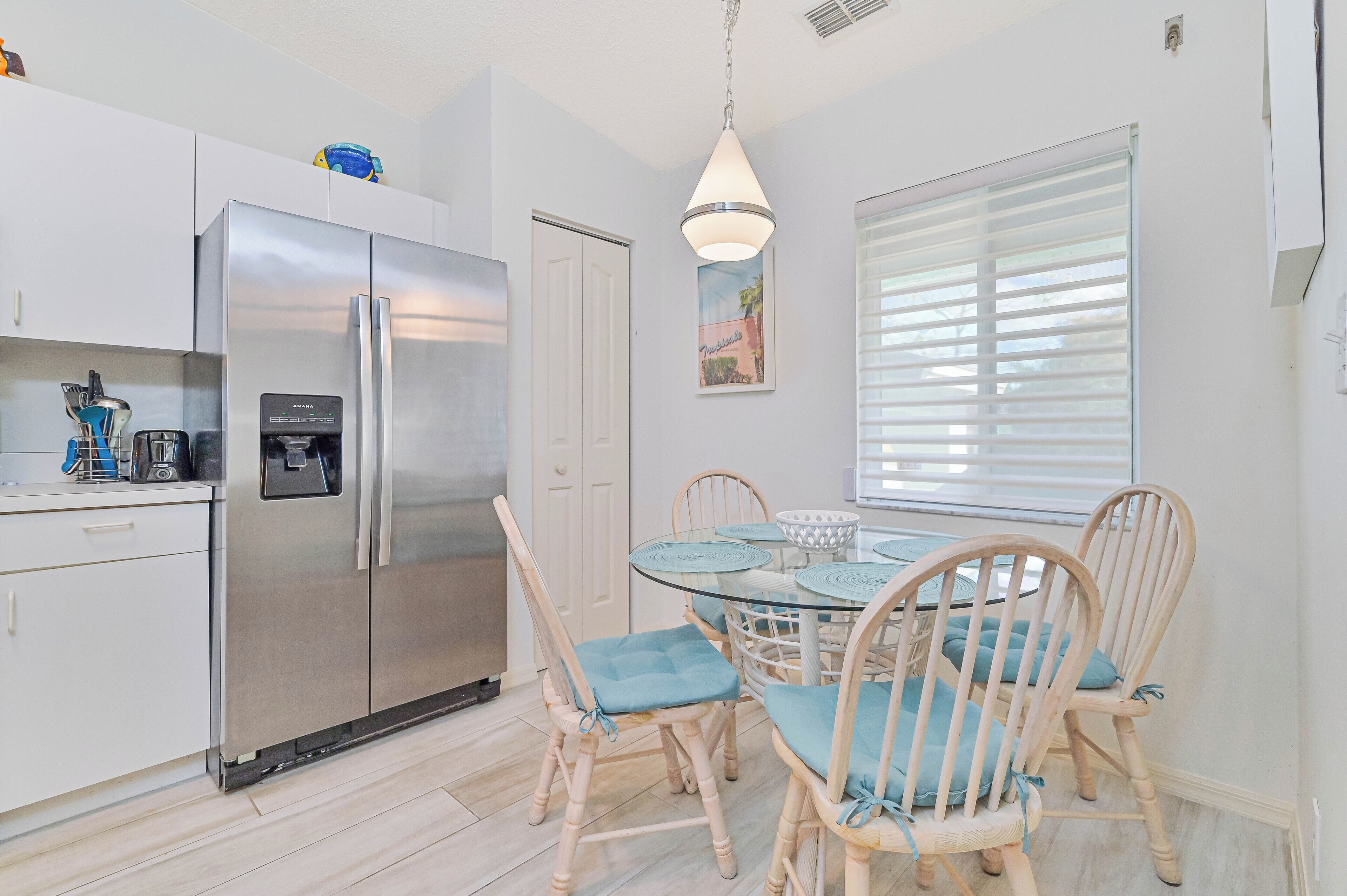 A modern kitchen with a stainless steel refrigerator, a water dispenser, and a dining area with a round glass table and wooden chairs.
