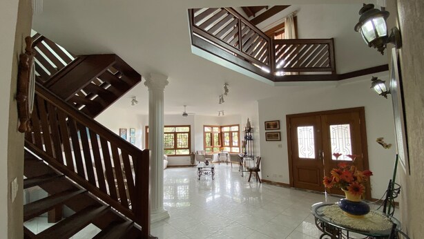 Ampla sala de estar com escada de madeira, mesa de jantar e um vaso decorativo.