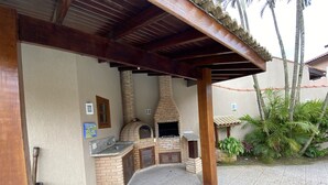 Uma área de cozinha externa com forno de tijolos, pia e pérgola de madeira.