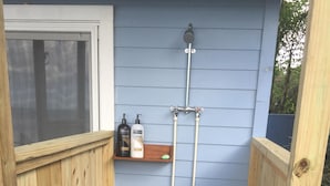 Een houten terras met een douchegedeelte, een houten plank met toiletartikelen en een houten mat.