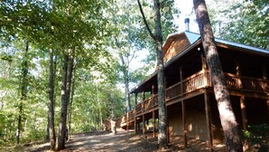 A wooden cabin with a covered porch and a chimney, surrounded by trees in a forested area.