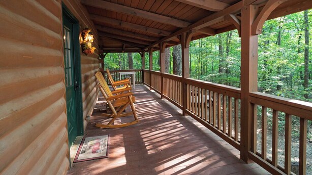 A wooden log cabin with a porch, rocking chairs, and a view of a forest.