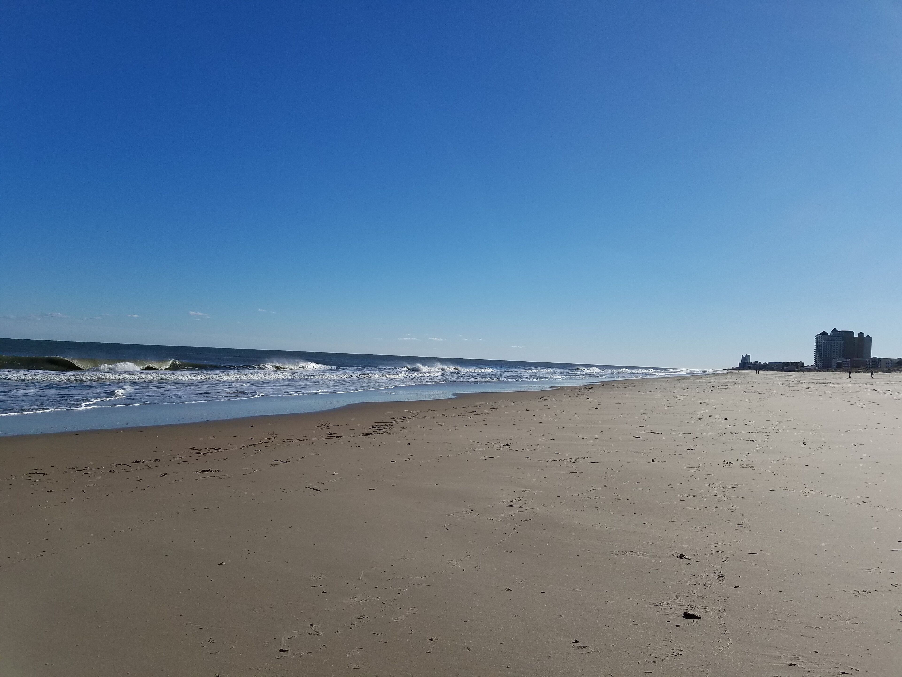 A beach with a clear sky, waves, and a building in the distance.