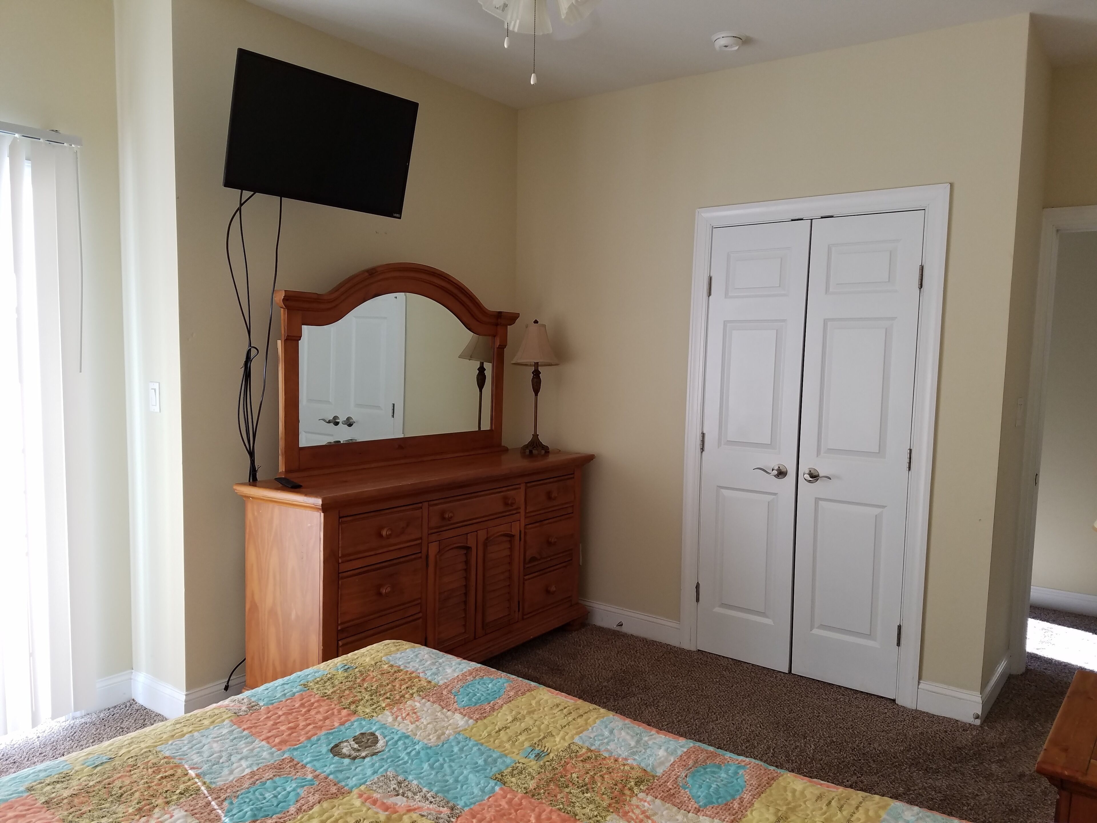 A bedroom with a wooden dresser, a mirror, a television mounted on the wall, and a door.