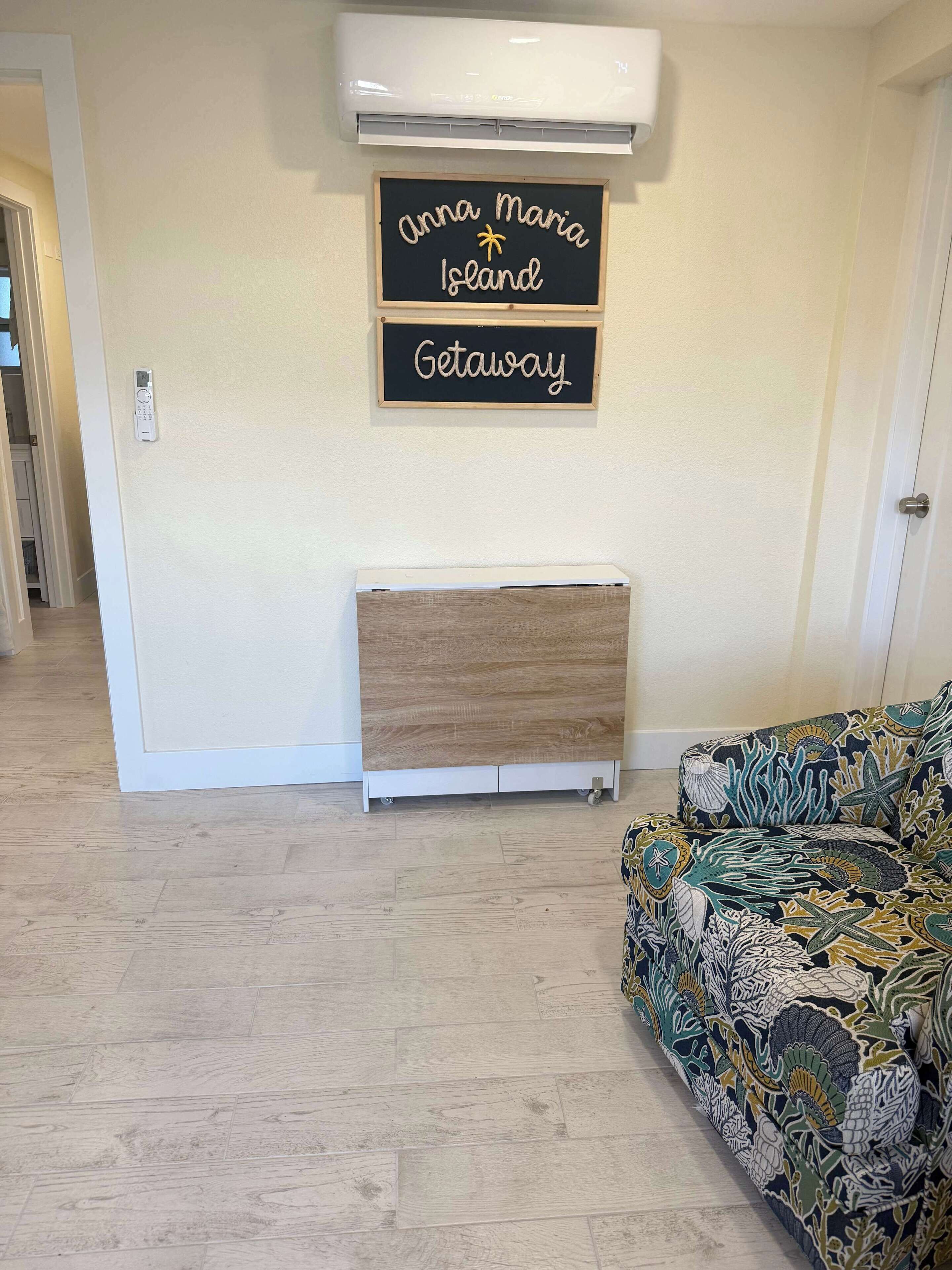Una habitación con piso de madera, un radiador blanco, aire acondicionado de pared y un letrero que dice "Anna Maria Island Getaway".