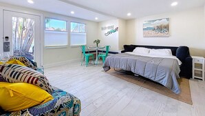A bedroom with a bed, a desk, and a chair. There is a window with blinds, a door, and a wall with a painting. - Bright Coastal Unit Steps From Beach/Walk 2 Bridge (bradenton beach)