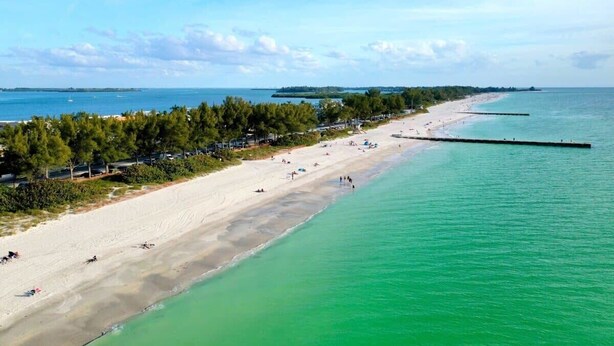A beach with clear turquoise water, a sandy shore, and a long pier extending into the sea. - Bright Coastal Unit Steps From Beach/Walk 2 Bridge (bradenton beach)
