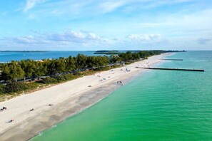 A beach with clear turquoise water, a sandy shore, and a long pier extending into the sea.