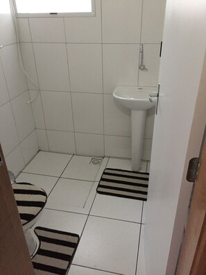 Um banheiro pequeno com azulejos, pia branca e vaso sanitário. Há dois tapetes listrados no chão.