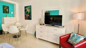 A modern hotel room with a flat-screen TV, white furniture, and two paintings on the walls.