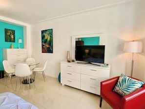 A modern hotel room with a flat-screen TV, white furniture, and two paintings on the walls.