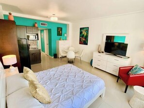 A hotel room with a bed, a TV, a desk, a chair, and a kitchenette.