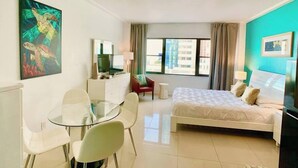 A hotel room with a bed, a desk with a chair, a TV, a painting, and a window with curtains.