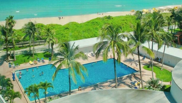 A pool with palm trees, a beach, and a view of the ocean.