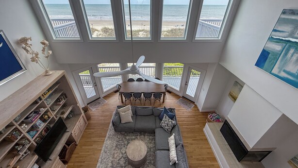 Un vaste salon doté d’une grande fenêtre donnant sur la plage, un coin repas et un espace salon confortable avec une cheminée.