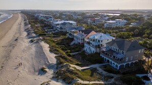 Un quartier résidentiel situé sur la côte, avec des propriétés en bord de mer, notamment des maisons à plusieurs étages dotées de balcons, une plage de sable et une vue dégagée sur l’océan.