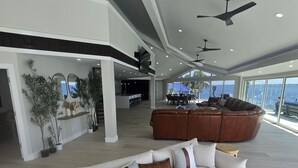 Een ruime woonkamer met een grote hoekbank, een houten bijzettafeltje en uitzicht op de oceaan.