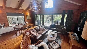 A cozy cabin-style room with a wooden interior, a dining area, and large windows offering a view of the outdoors.
