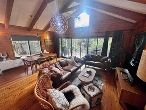 A cozy cabin-style room with a wooden interior, a dining area, and large windows offering a view of the outdoors.