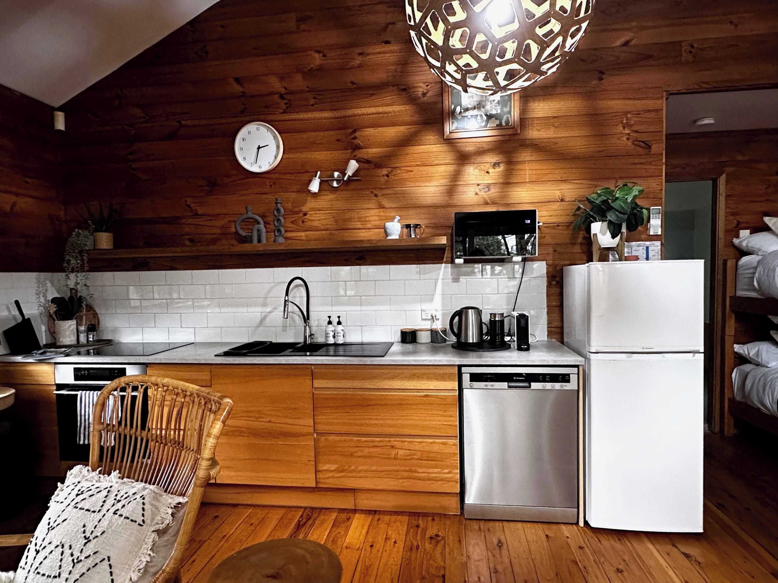 Een moderne keuken met houten wanden, een witte betegelde achterwand, roestvrijstalen apparatuur en een rieten stoel.