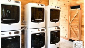 Une pile d’appareils électroménagers blancs, dont un sèche-linge et un lave-linge, dans une pièce en bois avec une porte en bois.