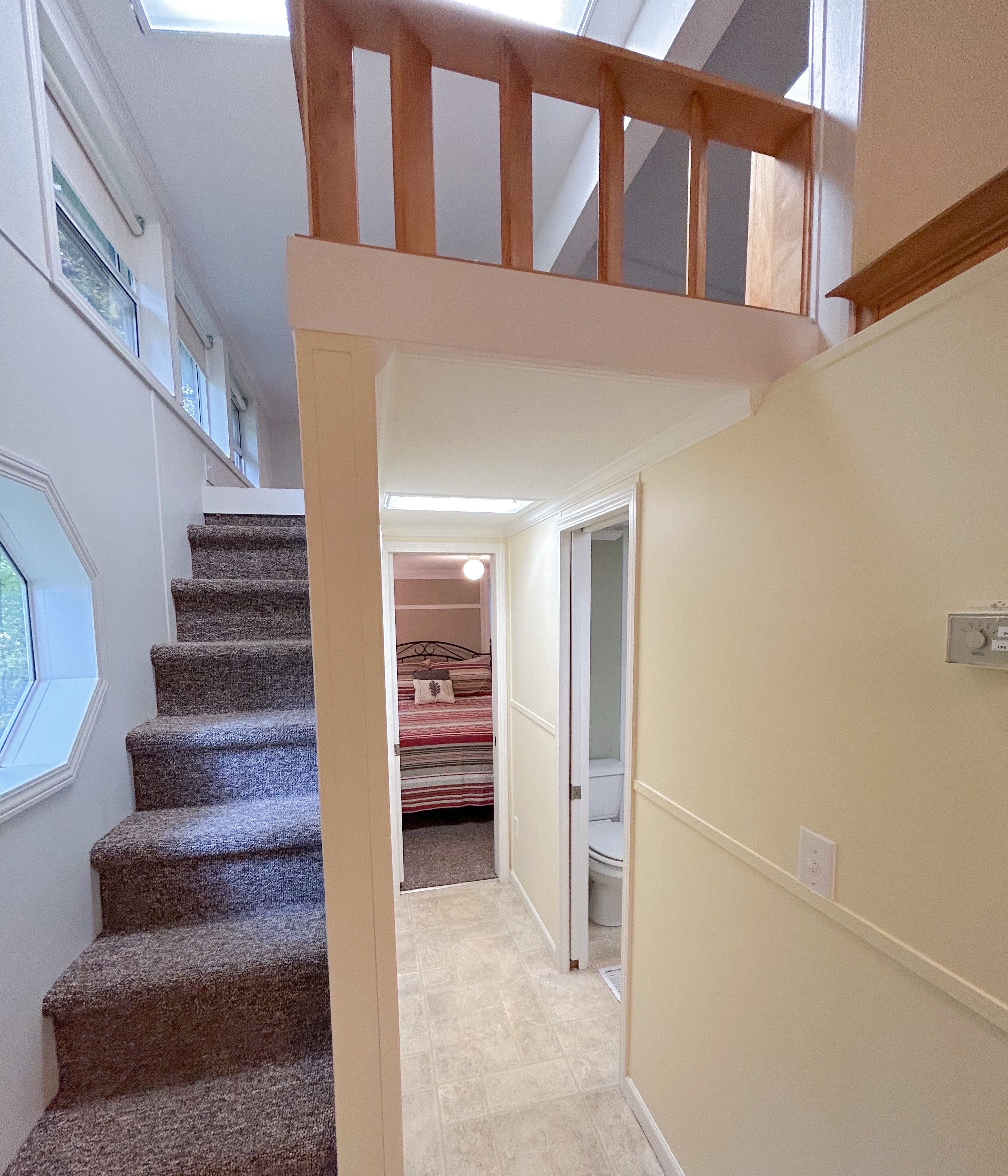 Un escalier menant à un deuxième étage, avec une rampe en bois, un placard contenant un lit et des toilettes visibles dans la pièce adjacente.