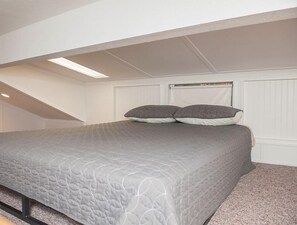 Een slaapkamer met een bed, schuine plafond en een raam met jaloezieën.