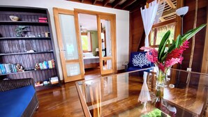 Un salón con suelo de madera, una mesa de centro de vidrio, una estantería y una cama al fondo.
