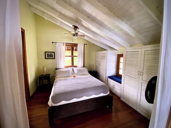 Un dormitorio con cama, ventilador de techo, ventana con cortinas y armario.