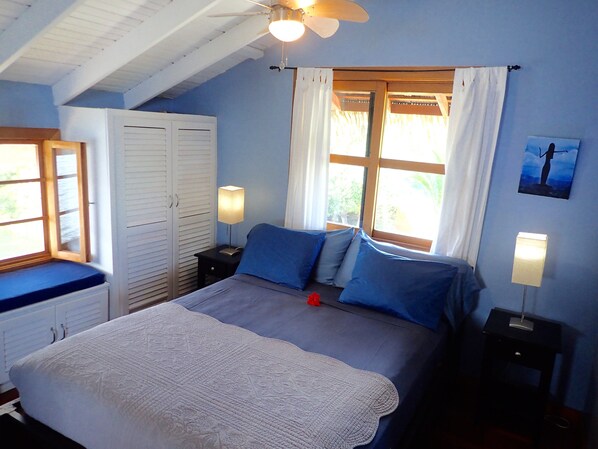 Un dormitorio con cama, mesita de noche, armario y ventana con cortinas.