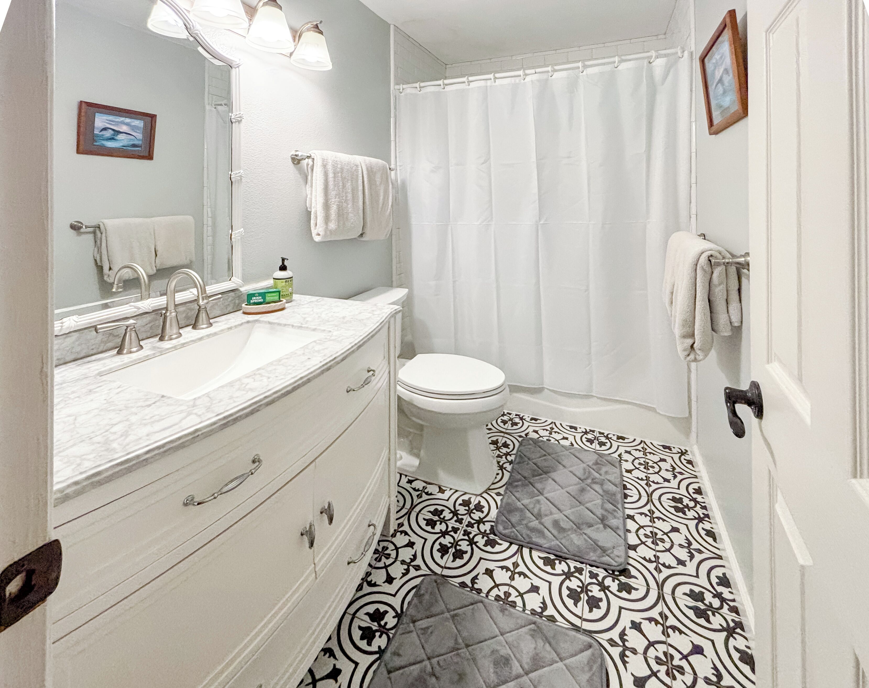 A bathroom with a white sink, mirror, and toilet, a patterned floor, and a shower curtain.