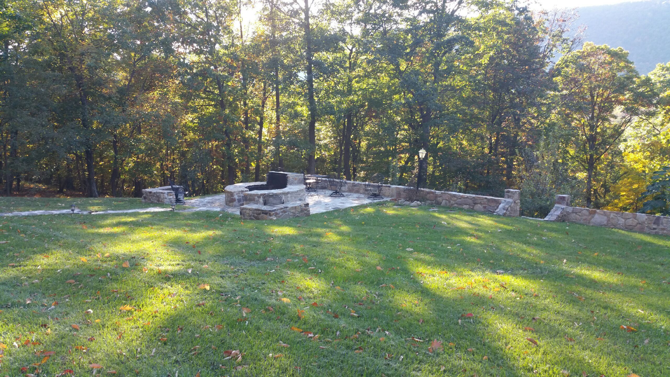 A stone patio with outdoor seating, surrounded by a grassy area and trees.