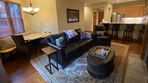 A modern living room with a black leather sofa, a wooden coffee table, and a dining area with a wooden table and chairs.