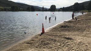 A sandy beach with a water body, a traffic cone, and a few people.